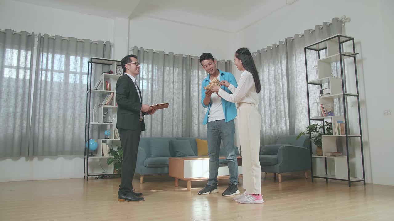 아시안 커플이 부동산 중개인으로부터 집 모델을 받은 후 엄지손가락을 올린 몸짓을 보여주는 전체 시각