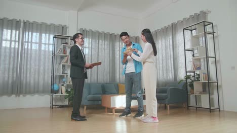 full view of asian couple showing thumbs up gesture after receiving the house model from a real estate agent in the house for sale