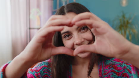 una joven feliz hace un símbolo de amor mostrando un corazón a la cámara para expresar sentimientos románticos
