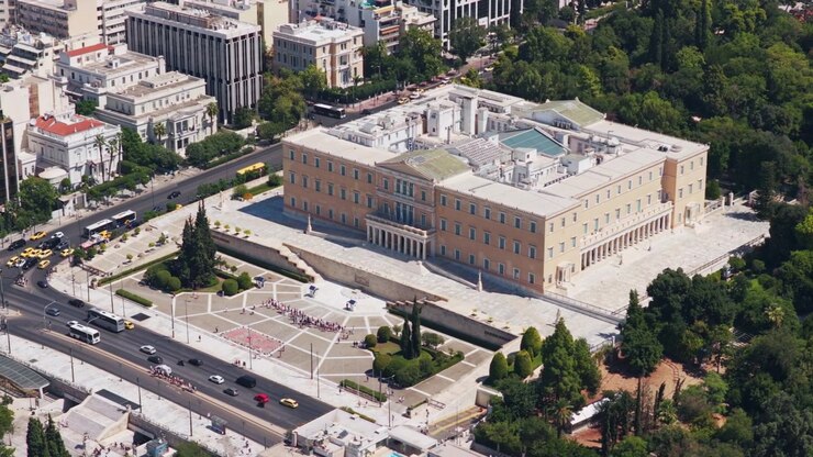 Vista aérea de ângulo elevado do histórico edifício do Parlamento Helénico e da Praça Syntagma no centro da cidade de Atenas, Grécia, com tráfego urbano a circular num dia de sol