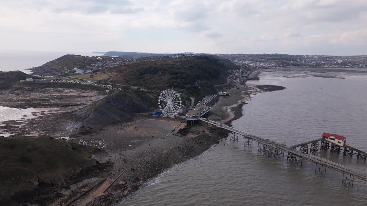 A high angle aerial pullback of Mumbles Pier, the Ferris wheel and ocean waves on a cloudy day