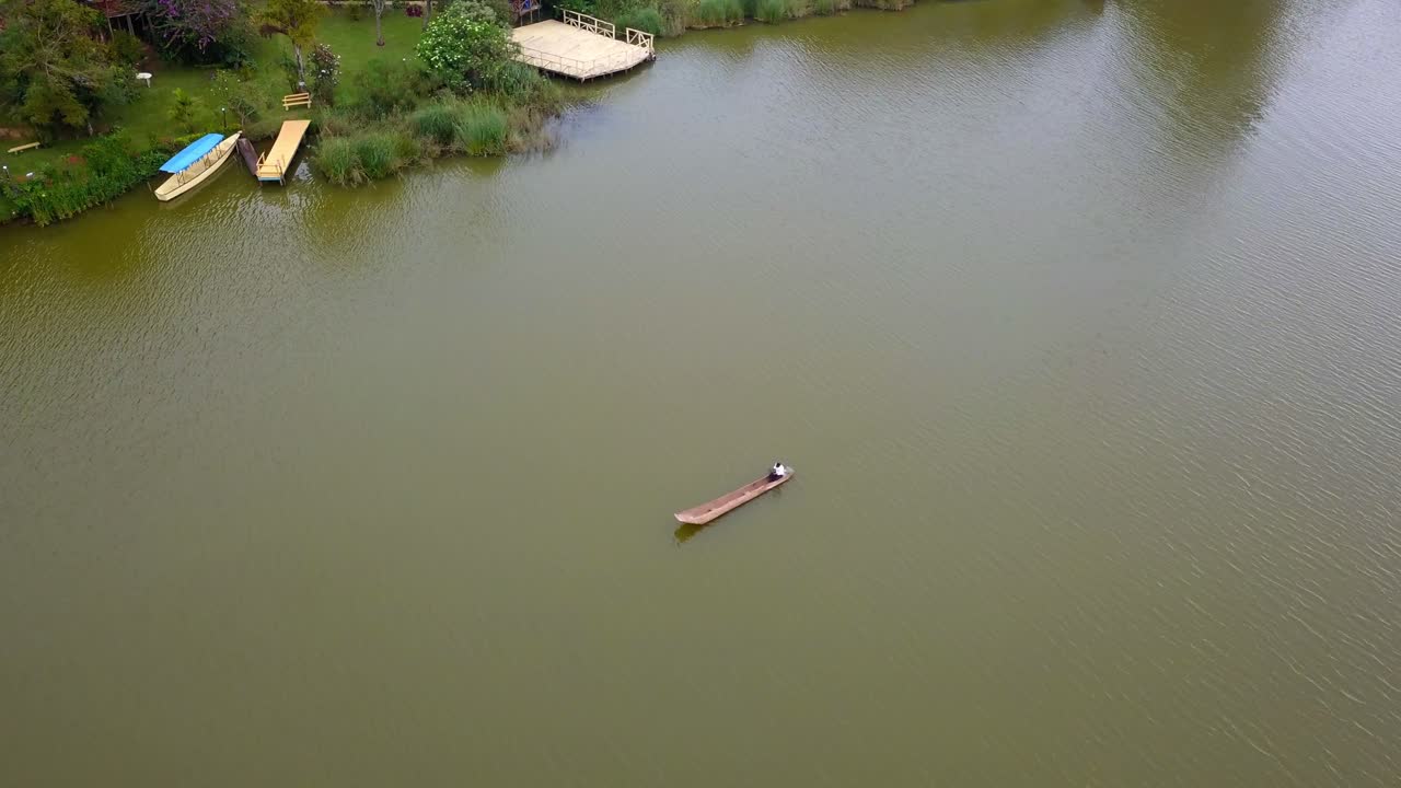 Drone view of a wooden dugout canoe on Lake Bunyonyi, Uganda, showing calm waters, shoreline vegetation, and lakeside community buildings