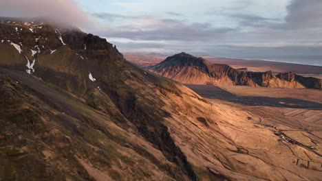 Aerial-panoramic-landscape-view-of-a-river-flowing-down-from-a-mountain-valley,-in-Iceland,-on-a-cloudy-evening