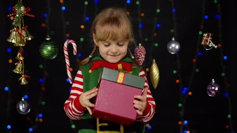 Kleines-Mädchen-Im-Weihnachtselfenkostüm-Als-Weihnachtsmannhelfer-Mit-Geschenkbox,-Blick-Hinein.-Schöne-Feiertage