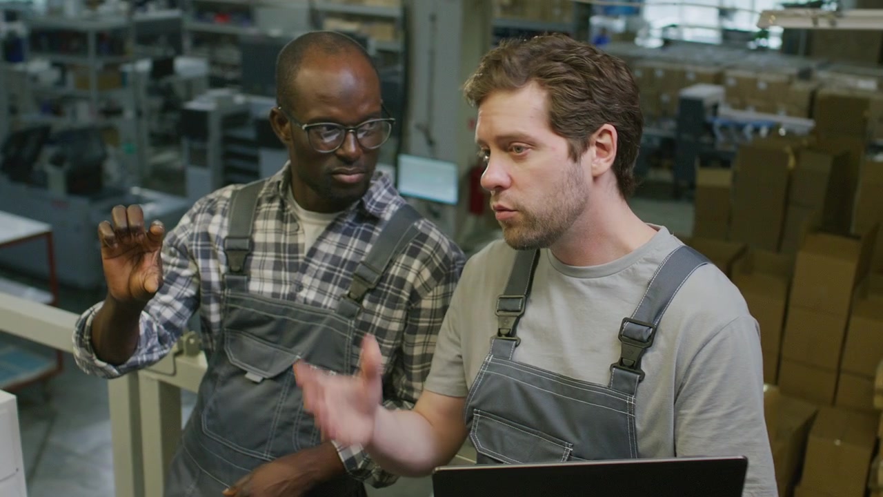 Multiethnic Technicians Discussing Manufacturing Process in Industrial Warehouse