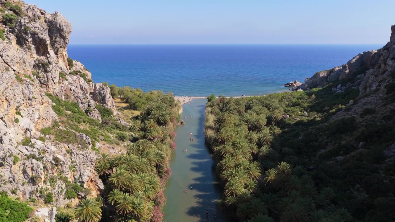 Letecký pohled dronem na pláž Preveli, kde se palmová řeka vlévá do moře vedle velké skály na oblázkovém pobřeží, Preveli, Řecko.