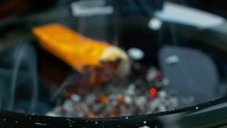 Close-up-view-of-an-ashtray-with-a-hand-crushing-and-extinguishing-a-cigarette,-nails-diseased-by-the-vice