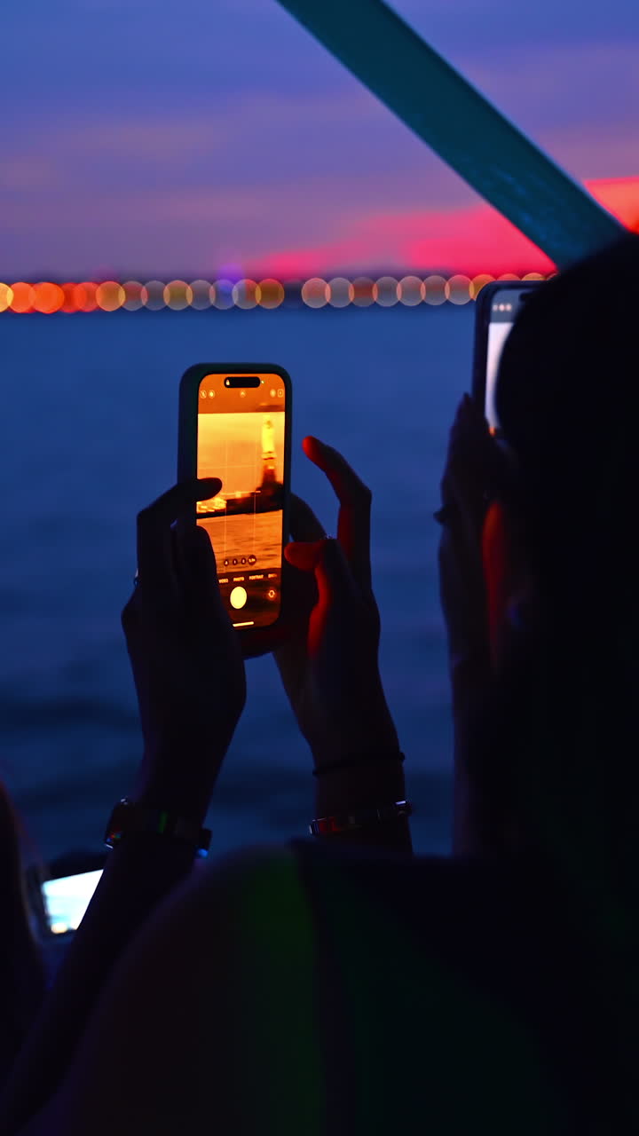 New York, USA, 8 agosto 2025: delle donne sono in piedi su una barca e tengono in mano dei telefoni. Alcuni turisti fotografano il bellissimo tramonto sul paesaggio acquatico. Video verticale