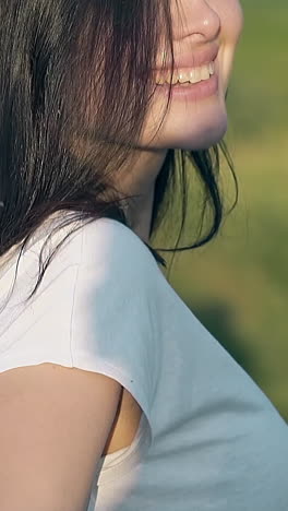 close view beautiful long haired brunette lady turns head with smile walking on green meadow slow motion