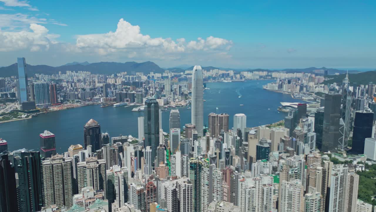 Aerial drone footage capturing Hong Kong city from Victoria Peak, showcasing skyscrapers, Victoria Harbour, and panoramic urban and coastal views