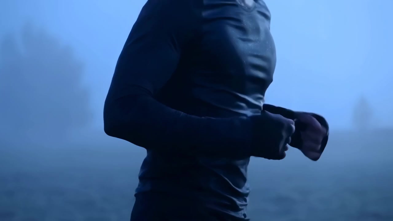 Vista lateral mostra uma pessoa a fazer jogging em terreno coberto por nevoeiro, com movimento rítmico, iluminação azul fria, paisagem distante desfocada e composição minimalista enfatizando o movimento e o exercício ao ar livre.
