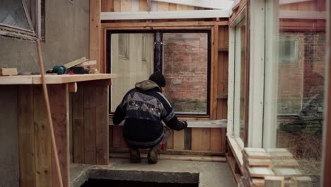 blick hinter männlichem arbeiter, der fensterbrett im gewächshaus misst