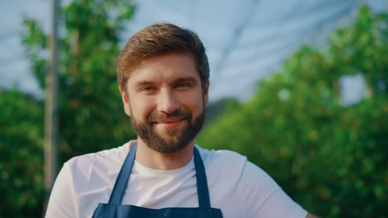 Professional farm worker smiling camera in summer orchard. Happy farmer posing.