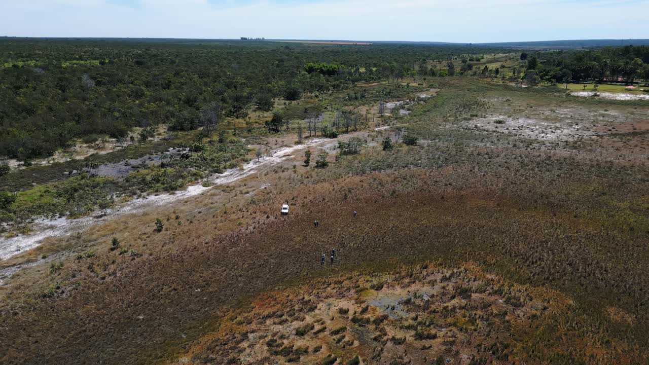 Bacino fluviale prosciugato nella savana del Cerrado brasiliano che mostra vegetazione degradata e un piccolo veicolo, a testimonianza delle sfide ambientali e della scarsità d'acqua che colpiscono i paesaggi naturali