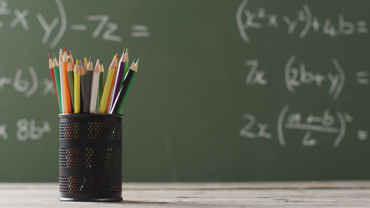 video de una taza con lápices de colores en una mesa de madera sobre fórmulas matemáticas en una pizarra