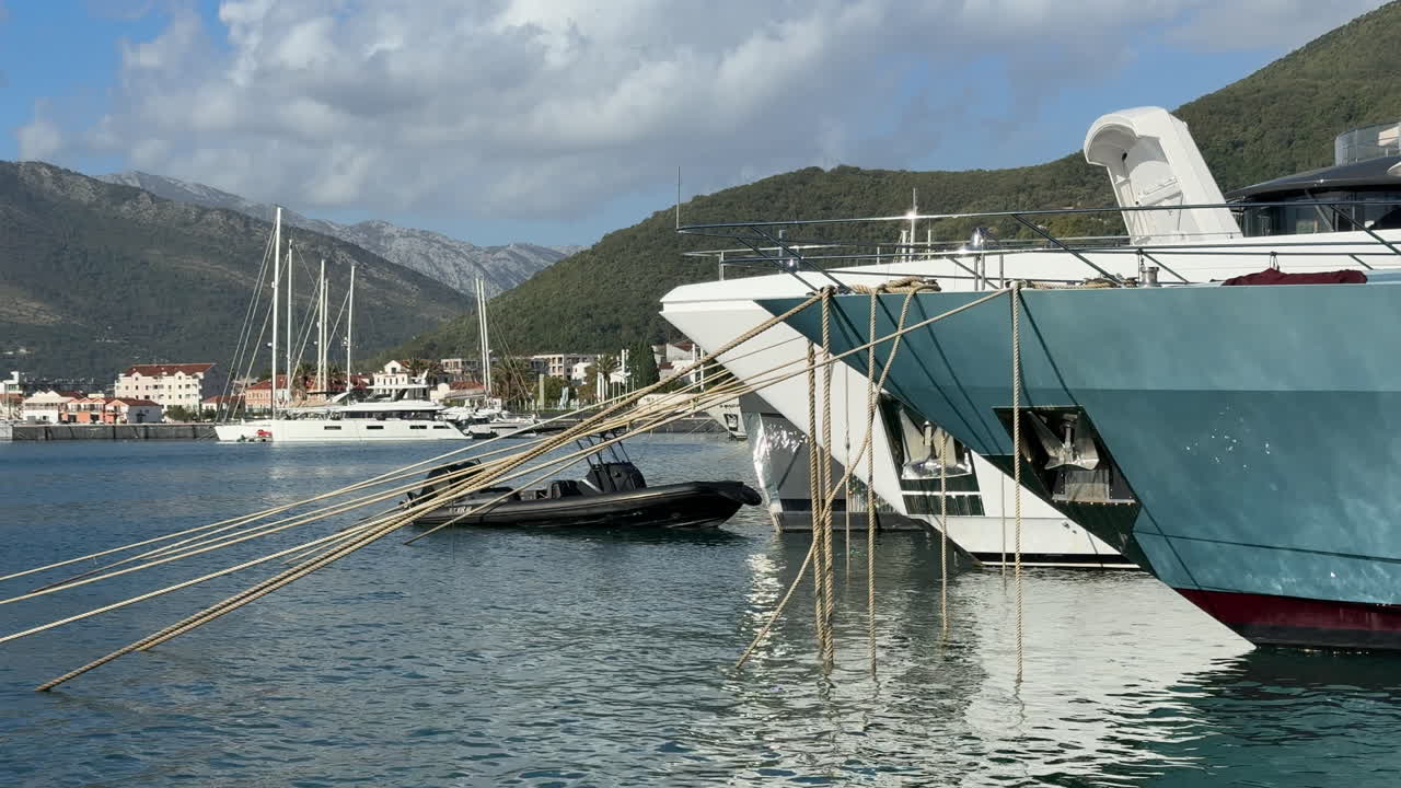 Close-up view of superyacht mooring ropes in Porto Montenegro, with luxury boats, calm Adriatic waters, and mountain scenery. Ideal for upscale travel, marina lifestyle, and nautical visuals