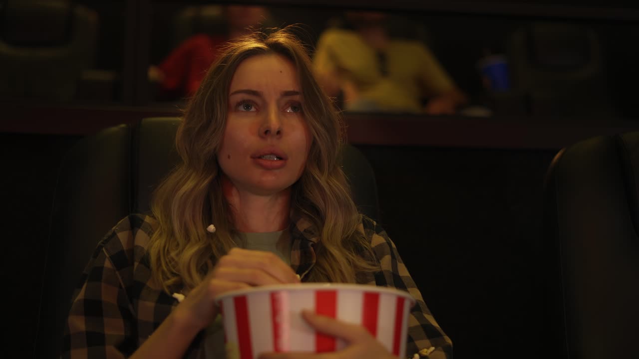 mujer sentada en un sillón viendo una película de terror en el cine, esparce la palomita de miedo