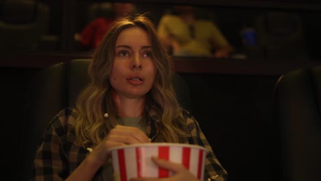 woman sitting in armchair watching a horror movie at the cinema, scatters the popcorn from fear