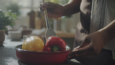 close-up of hands brushing oil on bell peppers in a kitchen