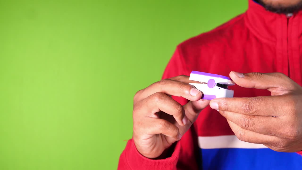 mano de un joven usando un oxímetro de pulso sobre un fondo verde