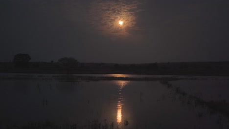 full moon rise over a lake with water reflection during night time in rural india
