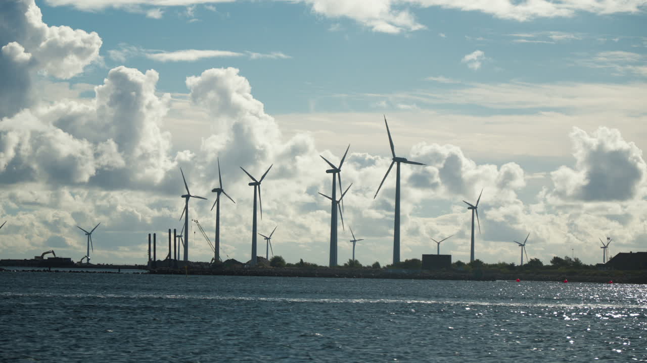 Majestic wind turbines against a cloudy sky over coastal waters. Perfect for renewable energy or environmental awareness videos.