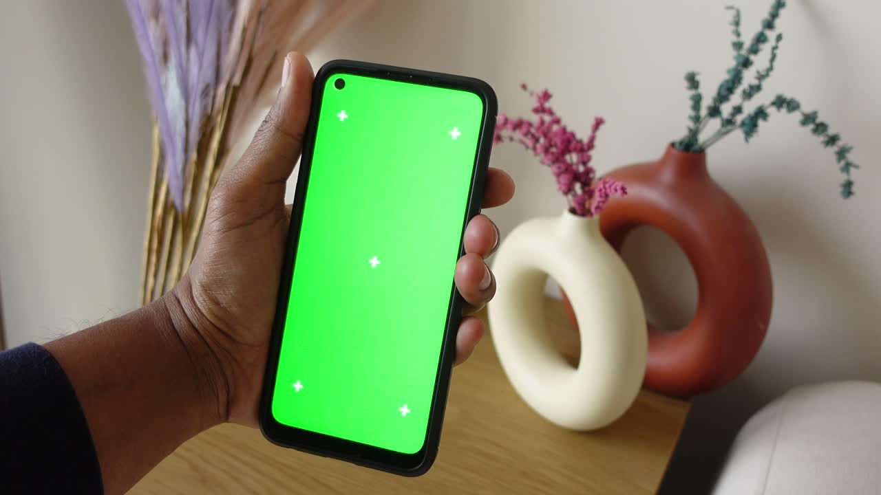 mano sosteniendo un teléfono inteligente con una pantalla verde y artículos decorativos