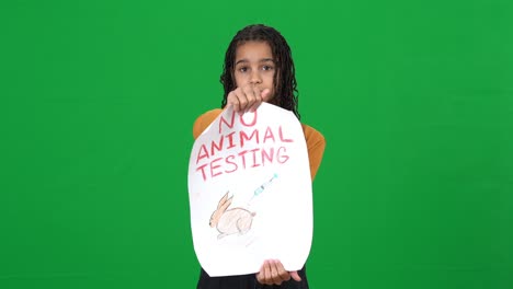 sad african american teen girl holding no animal testing message looking at camera with serious facial expression. portrait of conscious beautiful teenage activist posing on green screen chromakey.