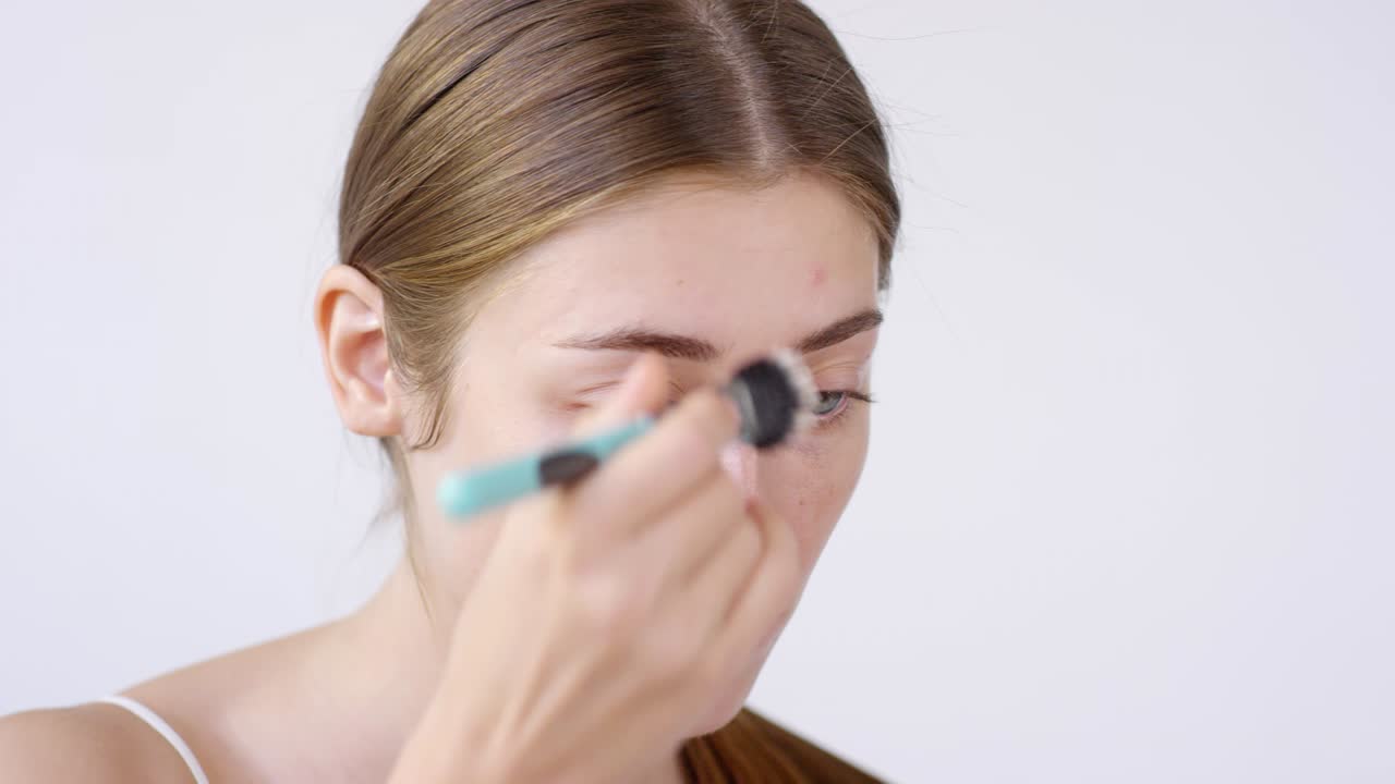 매력적인 여성이 메이크업 브러쉬로 프라이머를 적용하고 있습니다.