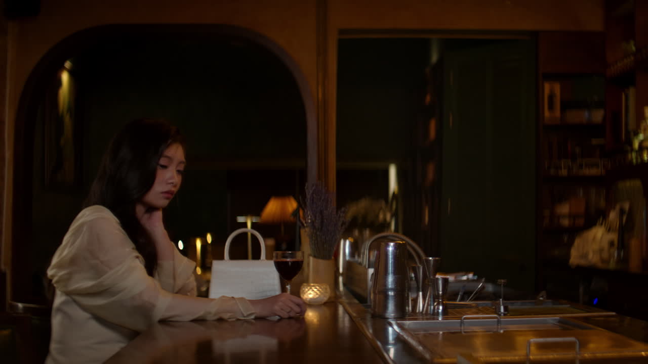 Sad woman sitting at a bar alone, looking down with a glass of wine in front of her
