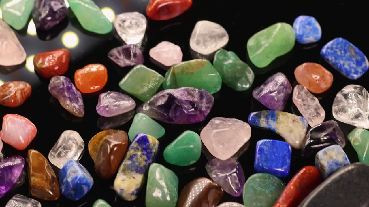 Colorful chakra stones gently shaking on a dark surface, highlighting their vibrant hues and polished textures