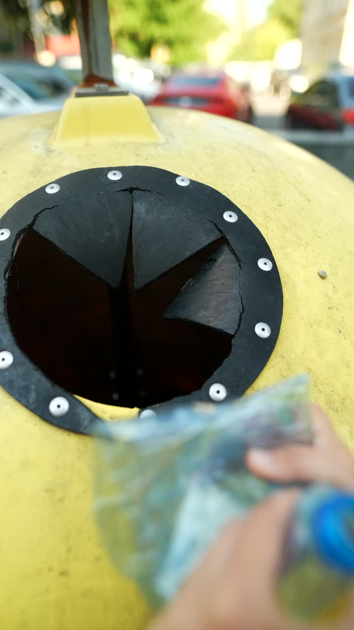 persona tirando basura en un contenedor de reciclaje amarillo