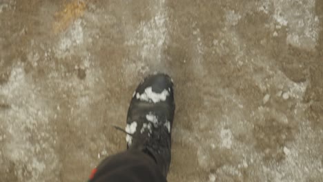 pov of man wearing black boots walking on frozen ground in winter