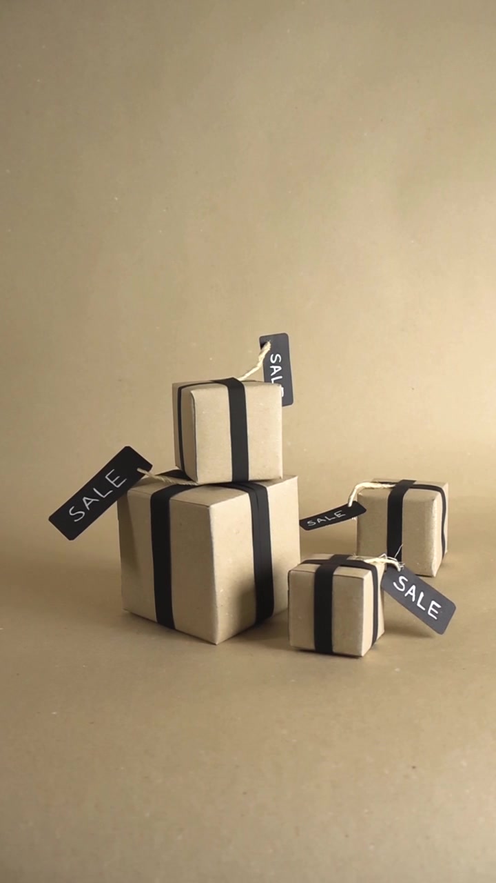 Several gift boxes wrapped in brown paper with black ribbons and sale tags slowly rotating on a seamless studio background. A perfect concept for holiday promotions, discounts, and e commerce
