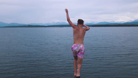 slow motion shot of a young man jumping off of diving board, into the ocean, shot taken from behind, looking down towards the man jumping, water splashing up as the man hits the water