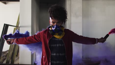 Mixed-race-man-holding-blue-and-purple-flares-standing-in-an-empty-building