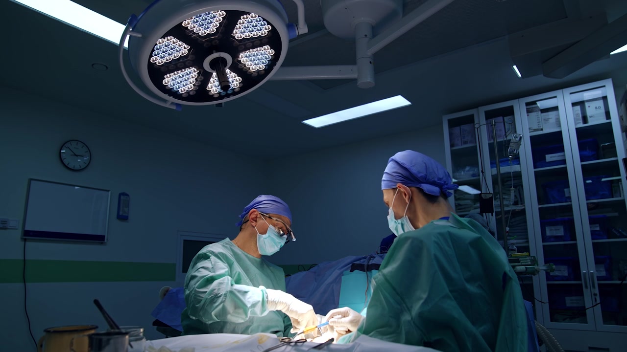 Læge iført kirurgiske lupper opererer patienten. Mandlig assistent forbereder værktøj til kirurgen