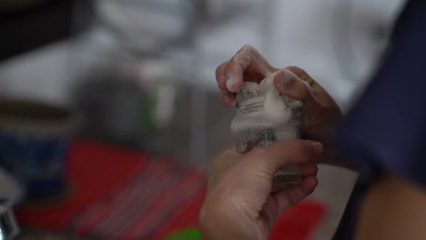 a man washes a small jar with a soapy sponge above a sink full of dirty dishes