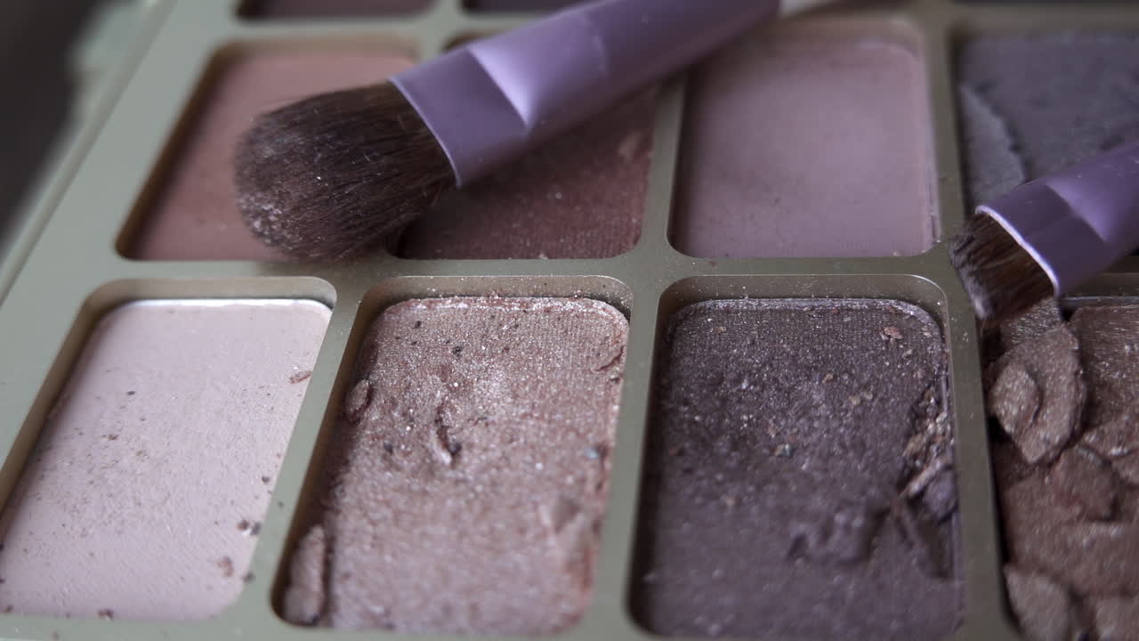 Close up of two purple make-up brushes on an eyeshadow palette