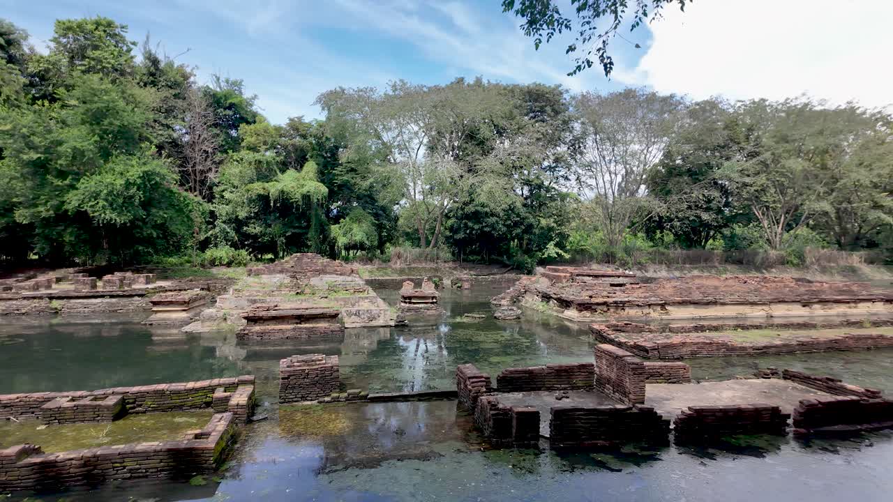 Wat Nan Chang ancient Buddhist temple ruins surrounded by water and lush green trees in Thailand. pan right