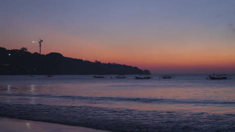 outrigger boats floating on the sunset open sea of jimbaran beach in bali, indonesia