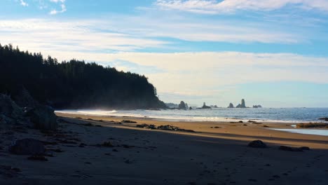 stunning drone time-lapse of the gorgeous third beach in forks, washington with large rock formations, surrounded by a pine tree forest on cliffs, and golden sand on a warm summer morning