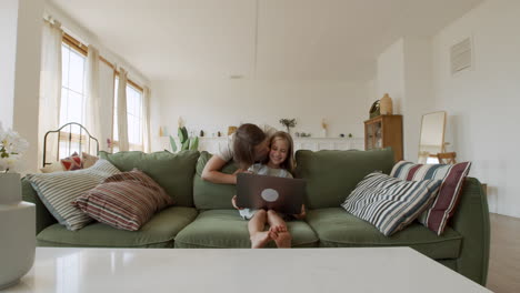 wide shot of a very affectionate mother who gives kisses to her responsible little daughter while she does her homework on the laptop