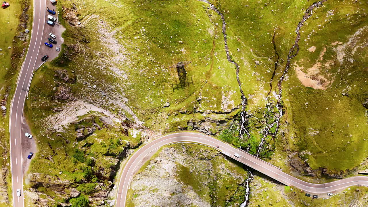 A bike follows a white car riding by the wavy mountain road. Rising over the Carpathian Mountains in Romania revealing view on the observation deck on Transfagarash highway