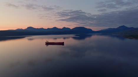 empty cargo ship anchored in calm fjord, vivid sunset sky reflection