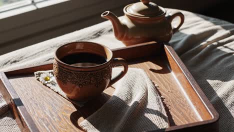 a cup of hot drink on a wooden tray by the window