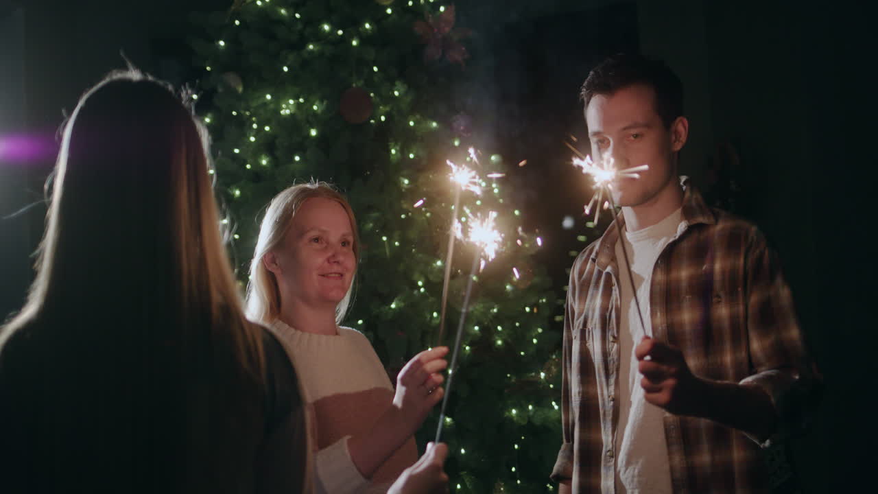 En glad familj firar nyår vid julgranen, hållandes brinnande tomtebloss.