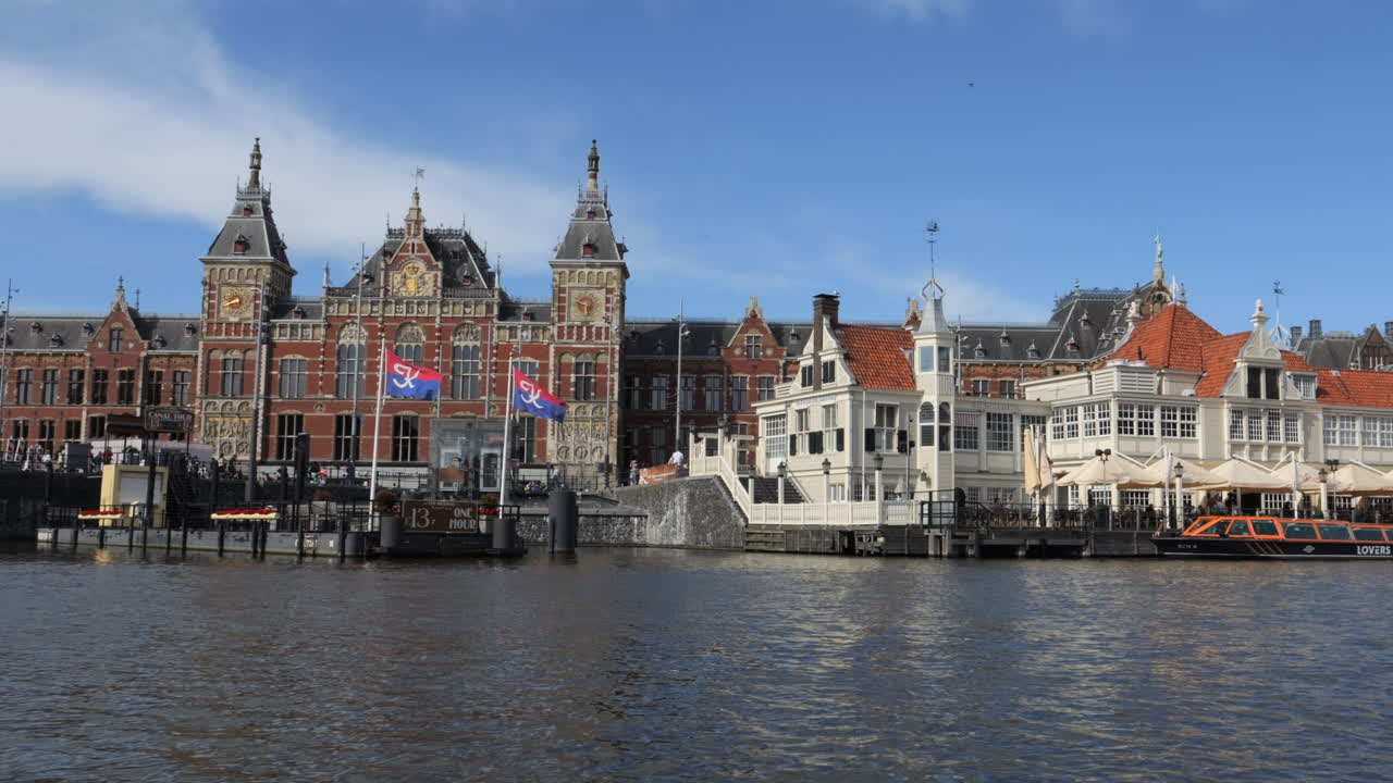 Amsterdam central station, a stunning architectural masterpiece, stands majestically on the oosterdok water, its reflection shimmering under the clear blue sky