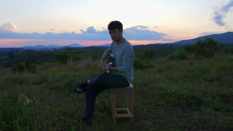 Músico-Masculino-Tocando-La-Guitarra-Al-Atardecer-Con-Montañas-Y-Horizonte-En-El-Fondo,-Vietnam