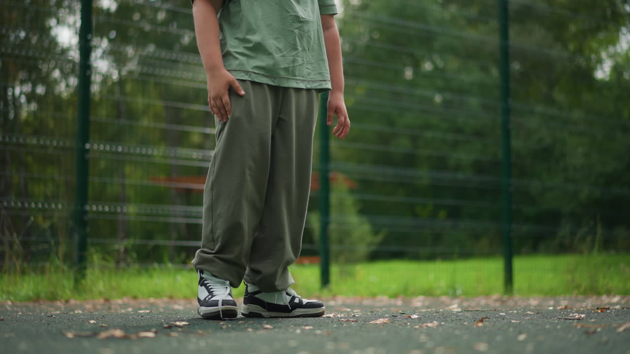 Boy Watches Dog In Park, Young Boy Observing Playful Dog Outdoors, Child In Park Interacts With Curious Dog Near Fence, Young Boy Stands On Court As Eager Dog Approaches His Legs And Sneakers
